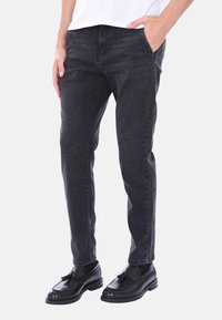 Jeans in denim nero con taglio dritto, caratterizzati da una leggera texture di lavaggio e tasche frontali, abbinati a scarpe in pelle nere.