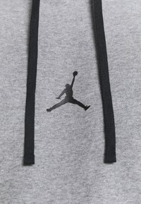 Logo Jumpman negro entre dos cordones de sudadera negros sobre un fondo de tela gris.