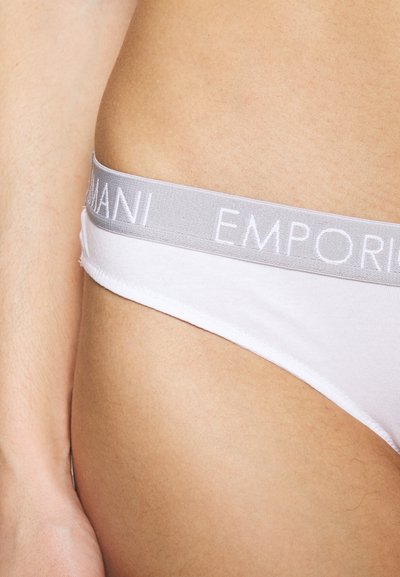 Fehér tangabugyi szürke rugalmas derékkal, amelyen az "EMPORIO ARMANI" dombornyomott felirat található. Puha anyag és sima felület.