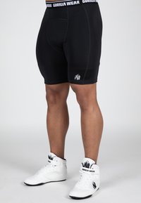 Zwarte sportieve shorts van rekbaar materiaal met een nauwsluitend ontwerp, met een wit "GORILLA WEAR" logo op de tailleband en een klein logo op het been.
