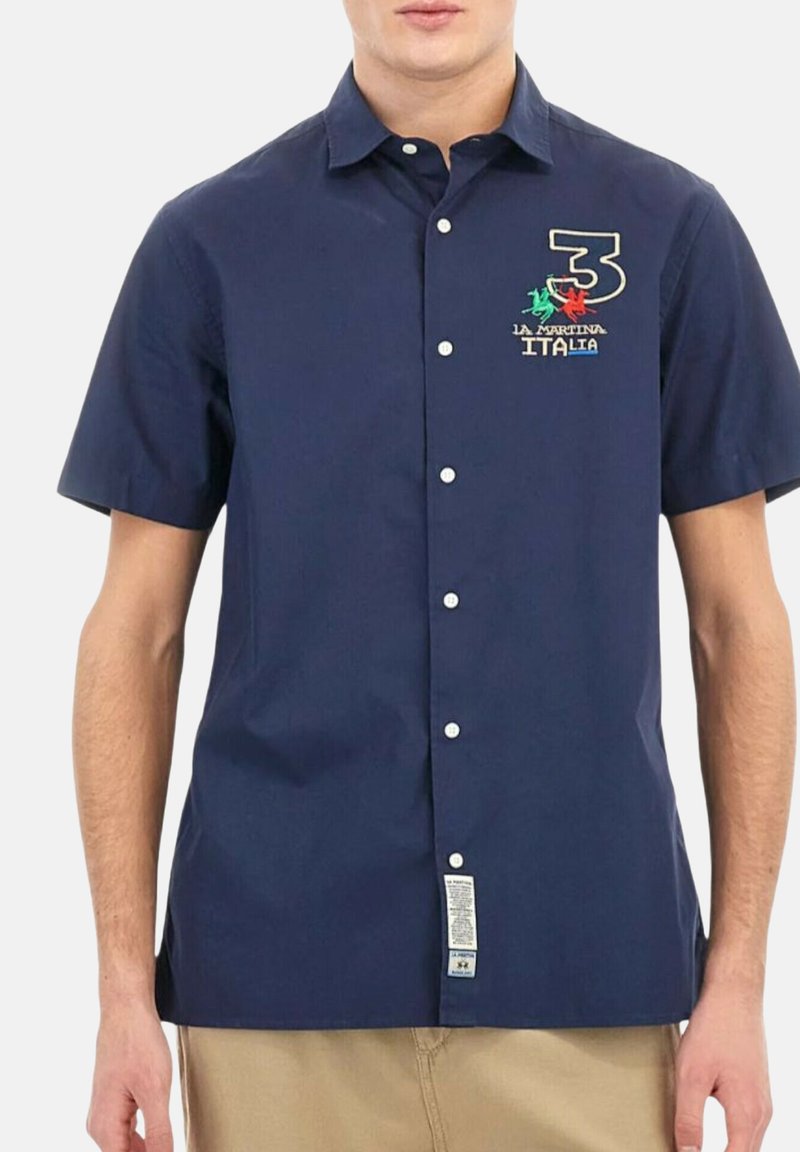 Man in een marineblauwe korte mouwen button-up shirt met geborduurd nummer 3 en een Italië-thema logo op de linkerborst.