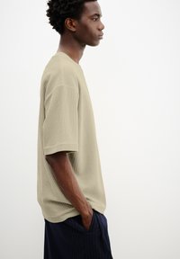 Beige struktureret T-shirt med en løs pasform, der har korte ærmer og rund hals, båret med navy-stribede bukser.