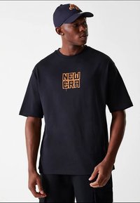 T-shirt preta de algodão com mangas curtas e gola redonda, com um logótipo laranja "NEW ERA" no peito. Corte casual.