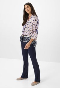 Blouse met meerdere patronen in roze, blauw en marineblauw, met een geometrisch ontwerp; gecombineerd met marineblauwe broek en taupe flats.
