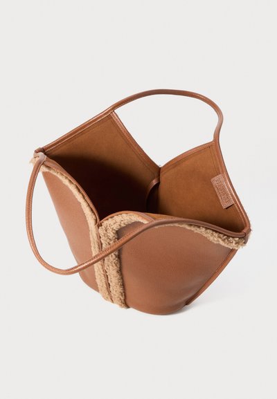 Brown leather handbag with shearling trim, open top, and slim handles against a plain white background.