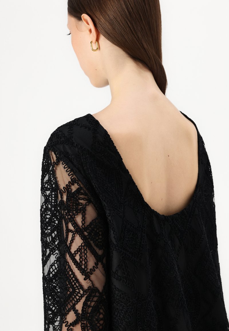 Top de encaje negro con un escote en V profundo en la parte de atrás y patrones florales texturizados. Mangas de tela transparente con intrincados detalles de bordado.