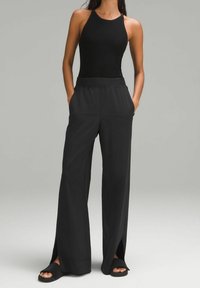 Zwarte geribde tanktop gecombineerd met wijde zwarte broek met zijsplitten, een gladde textuur en een elastische tailleband. Zwart instap-sandalen.