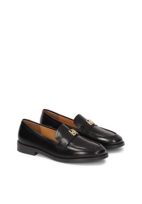 Melni ādas loafers ar noapaļotu purngalu, zelta logotipa akcentu uz joslas un zemu, izturīgu papēdi. Gluda apdare ar minimālām šuvju detaļām.