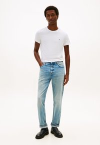 Wit katoenen T-shirt met een klein logo, lichtblauwe denim jeans met een losse pasvorm en zwarte schoenen; minimalistisch ontwerp en casual stijl.