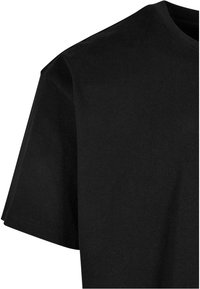 T-shirt noir en coton à manches courtes et col rond montrant le haut du torse et la zone des épaules.