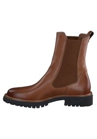 Botas de tobillo de cuero marrón con paneles laterales elásticos, punta redonda y una suela de goma negra gruesa. Costuras detalladas a lo largo del borde.