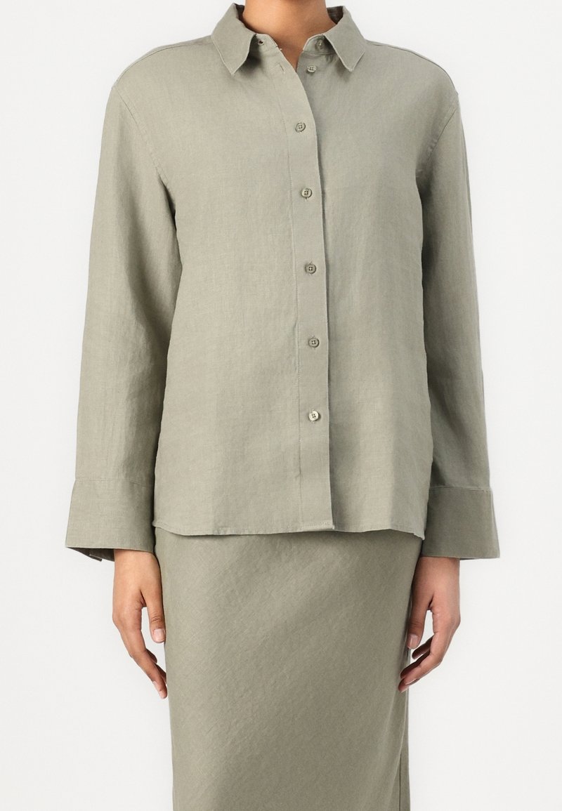 Chemise boutonnée vert clair en tissu texturé, avec un col et des manches longues munies de larges poignets.