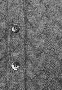 Hallide hallitusseente muster, tekstureeritud pind ja kaks ümmargust musta nööpi esitlev hall kudumikaelus. Suurendatud vaade toob esile detailid.