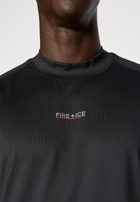 Czarna koszulka sportowa z krótkim rękawem o prążkowanej teksturze, z małym logo "FIRE + ICE" w białym i czerwonym kolorze na klatce piersiowej.