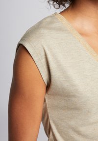 Beige kortärmad topp med V-ärm, som har en subtil metallictråd på halsringningen och ett mjukt, texturerat tyg.