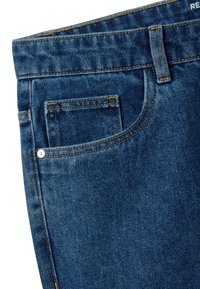 Primer plano de unos vaqueros de mezclilla azul que muestran el bolsillo delantero, el bolsillo para monedas, la presilla para el cinturón, costuras naranjas y detalles de remaches metálicos.