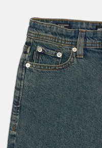 Jeans de mezclilla azul extra holgados con costuras naranjas contrastantes, diseño de cinco bolsillos y herrajes metálicos plateados en la parte frontal.