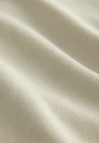 Jasno beżowy materiał o gładkiej, lekko błyszczącej strukturze. Widoczny wzór tkany, tworzący miękki, falujący wygląd.