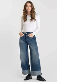 Jeans di denim a gamba larga con risvolti arrotolati, caratterizzati da una tonalità azzurro chiaro e design a cinque tasche, abbinati a un top bianco aderente a maniche lunghe.