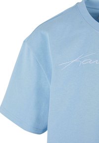 T-shirt en coton bleu clair à coupe décontractée, à manches courtes, col rond, et logo 'Karu' brodé en blanc sur le devant.