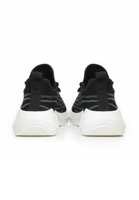 Scarpe sportive nere in maglia con una parte superiore testurizzata e strisce grigie, e una suola in gomma bianca. Presentano un'etichetta per il supporto sul retro.