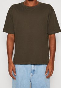 Olive green cotton t-shirt, crew neck, relaxed fit, short sleeves, stitched hems, paired with light blue denim shorts, minimal branding detail.