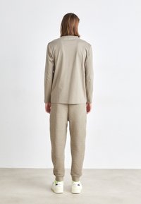 Camisa de manga comprida bege combinada com calças de moletom bege texturizadas com um padrão hexagonal, usadas com ténis brancos e detalhes amarelos.