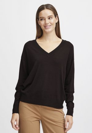 Black v-neck sweater with long sleeves, relaxed fit, ribbed cuffs, and hem. Worn with beige pants. Soft texture, casual design.