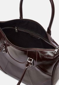 Borsa a mano in pelle bordeaux con finitura lucida, zip superiore e doppio manico. L'interno presenta una fodera in tessuto scuro e una tasca con zip.