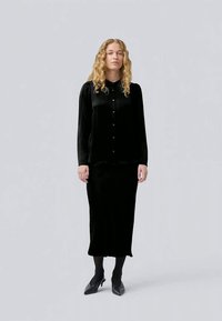 Black velvet blouse with button closure paired with a long black skirt. Elegant silhouette, smooth texture, and minimalistic design.