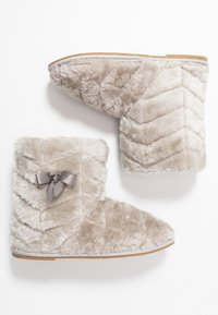 Bottes gris clair floues avec texture en chevrons, bout arrondi et détail de nœud sur le côté. Matière douce et pelucheuse avec une semelle plate.
