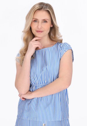 Lyshåret kvinde med bølget hår iført blå og hvidstribet top med korte ærmer poserer med hånd på hagen mod en hvid baggrund.
