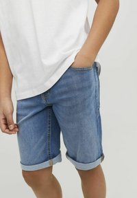 Shorts de denim en azul claro, con dobladillos enrollados, corte casual y costuras visibles. Combinados con una camiseta blanca.