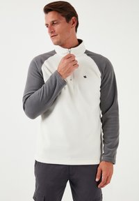 Fleece pullover med halvlukning, med hvid krop og grå raglanærmer. Inkluderer et lille logo på brystet, glat tekstur.