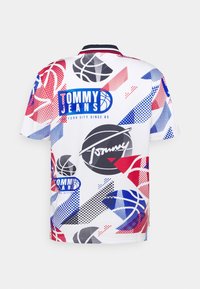 Koszulka krótki rękaw w kolorze białym, w stylu koszykarskim, z czerwonymi, niebieskimi i czarnymi geometrycznymi wzorami, logo i kropkowanymi detalami.