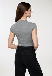 Maglietta grigia aderente a maniche corte abbinata a jeans neri a vita alta. La maglietta ha una texture liscia; i jeans presentano due tasche posteriori.