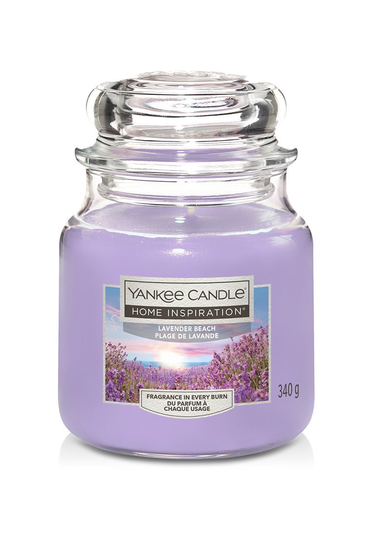 Candela profumata alla lavanda in un barattolo di vetro trasparente, con interno in cera viola e un'etichetta argento con immagini floreali. 340 g.
