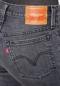 Vaqueros de mezclilla negra con una etiqueta de piel marrón de Levi Strauss & Co. y una etiqueta roja en el bolsillo trasero, que muestran un diseño clásico.