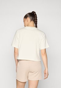 Gekürztes cremefarbenes T-Shirt mit kurzen Ärmeln, aus weichem Baumwollstoff, kombiniert mit beigen Ripp-Shorts, die ein einfaches, lässiges Design hervorheben.