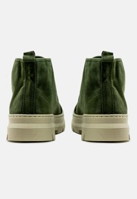 Botas de tobillo de tela verde con superficie texturizada, con una suela beige gruesa y una lengüeta en la parte posterior para facilitar su uso.