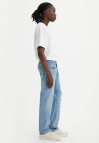 Camiseta de algodón blanca, jeans de mezclilla azul clara, corte relajado, diseño sencillo, combinada con zapatos de colores claros. Vista de perfil.