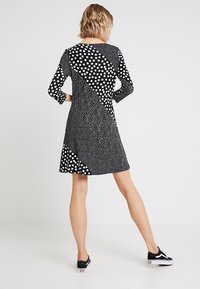 Robe noire et blanche à manches longues, présentant un design géométrique avec des motifs de points variés et des textures contrastées, avec un ourlet évasé.