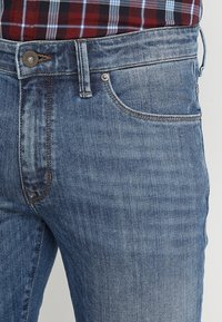 Light blue denim jeans with a slim fit, featuring a five-pocket design, visible stitching, and a metal button closure at the waist.