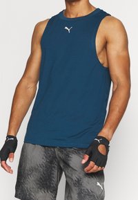Nachtblau, mouwloze sporttank top gemaakt van zacht stof. Heeft een klein wit logo op de borst en wordt gecombineerd met grijze, gemusterde shorts.
