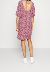 Červené a modré šaty se vzorem, krátkými puff rukávy, nízkým výstřihem na zádech a zavazováním. Dokončeno s bílými teniskami pro ležérní vzhled.