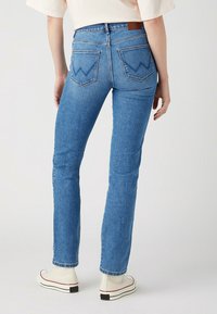 Siniset farkut, joissa on kapea malli, viisi taskua ja zigzag-ommeltu taustatasku. Yhdistetty valkoisiin korkeisiin tennareihin.