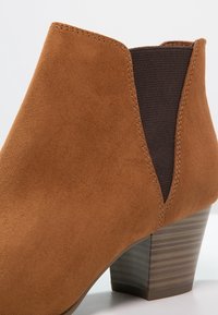Bottine en suède marron avec talon bloc en bois empilé et panneau élastique latéral foncé pour un enfilage facile.