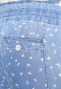 Helle blaue Shorts aus weichem Material mit einem weißen Vogelmuster. Mit einem elastischen Bund und einer einzelnen Gesäßtasche mit einem Knopf.