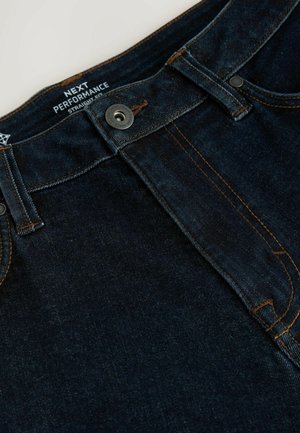 Blugi din denim de culoare albastru închis, cu croială dreaptă, având cusături portocalii, un nasture metalic și eticheta de marcă pe talie.