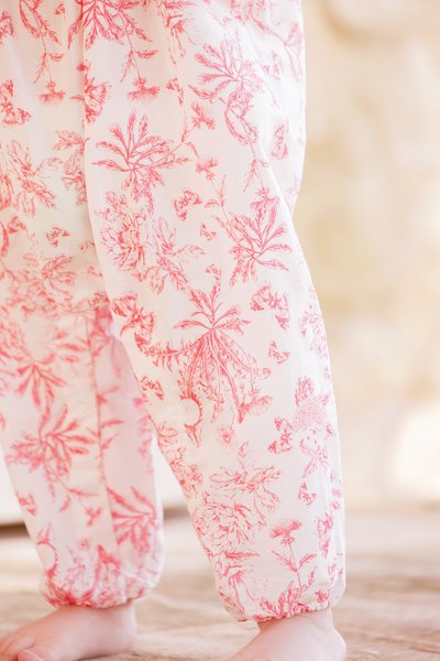 Calças leves com padrão floral em rosa suave com desenhos botânicos em vermelho. Apresentam punhos elásticos e um corte descontraído para conforto.